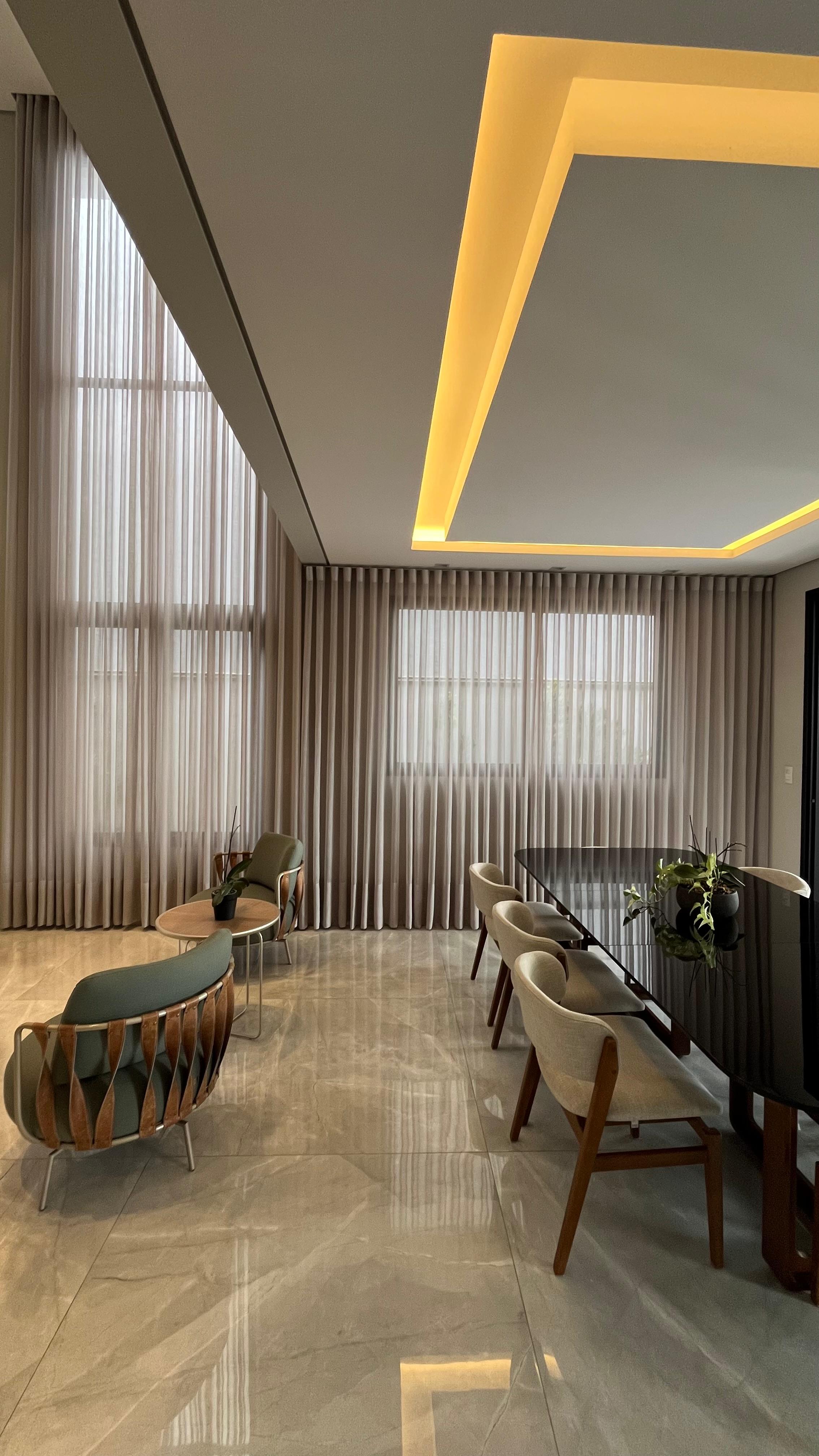 Sala de estar de pé direito alto com cortina de voil e poltronas verdes